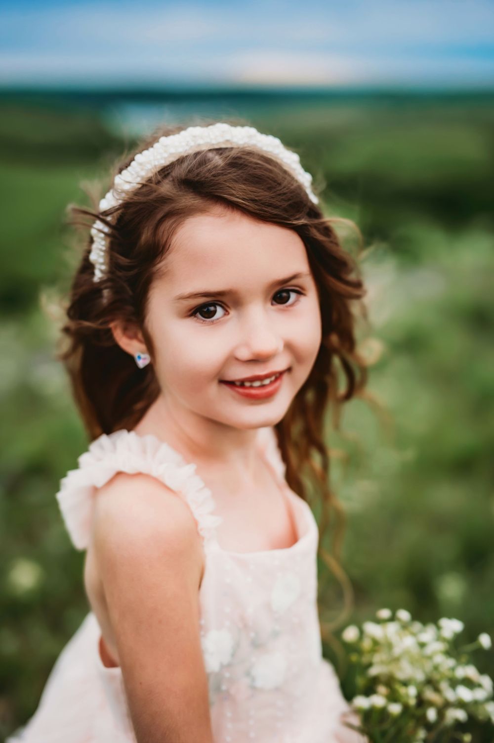 Beautiful outdoor photoshoot showing a child in a white lace dress with flowers in the background.