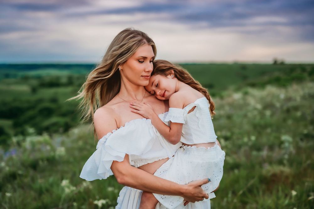 Family embraces lovingly in a wildflower meadow wearing white dresses during golden hour at sunset.