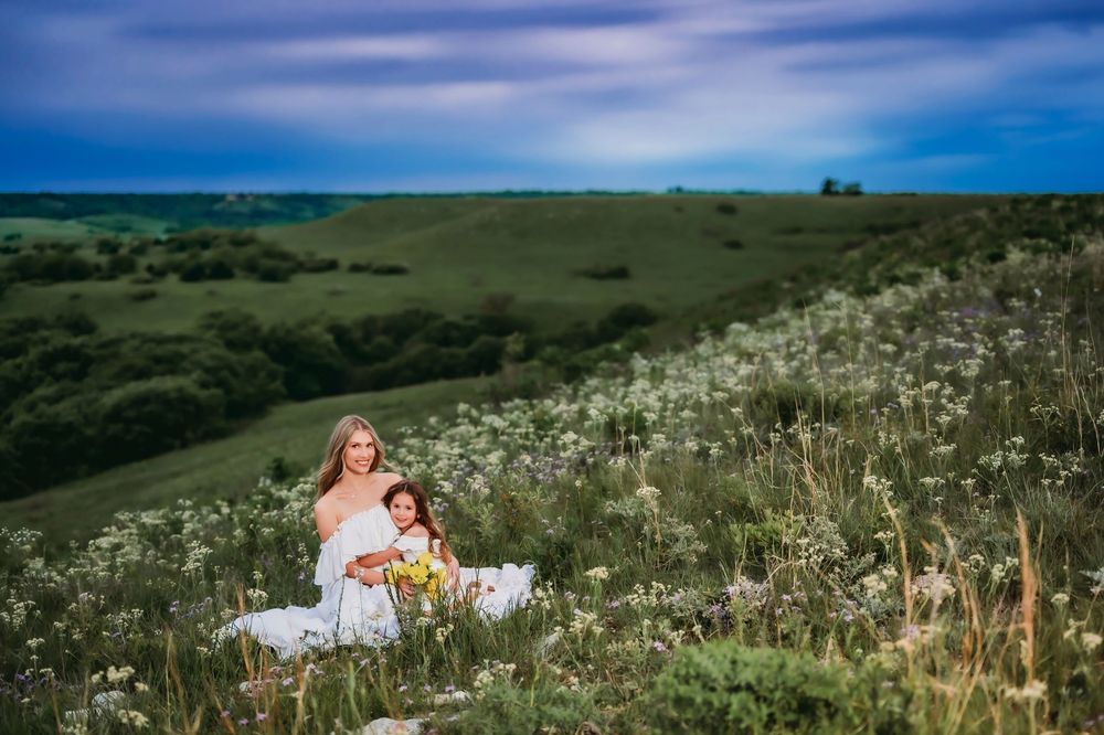 Rolling green hills covered in wildflowers stretch into the distance on a sunny day with dramatic blue sky overhead.