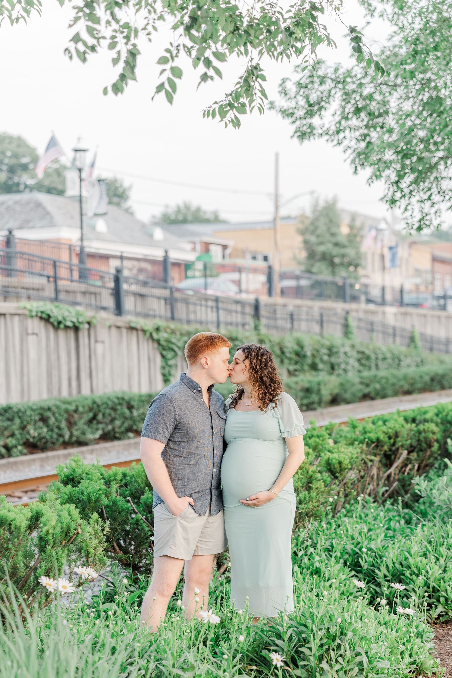 A couple poses in an urban garden setting with buildings visible in the background.