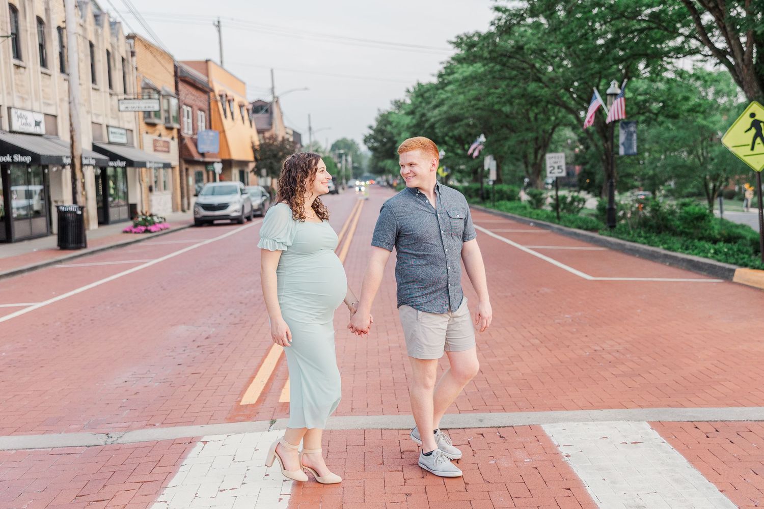 A couple walks hand in hand down a brick-paved street during their maternity session.