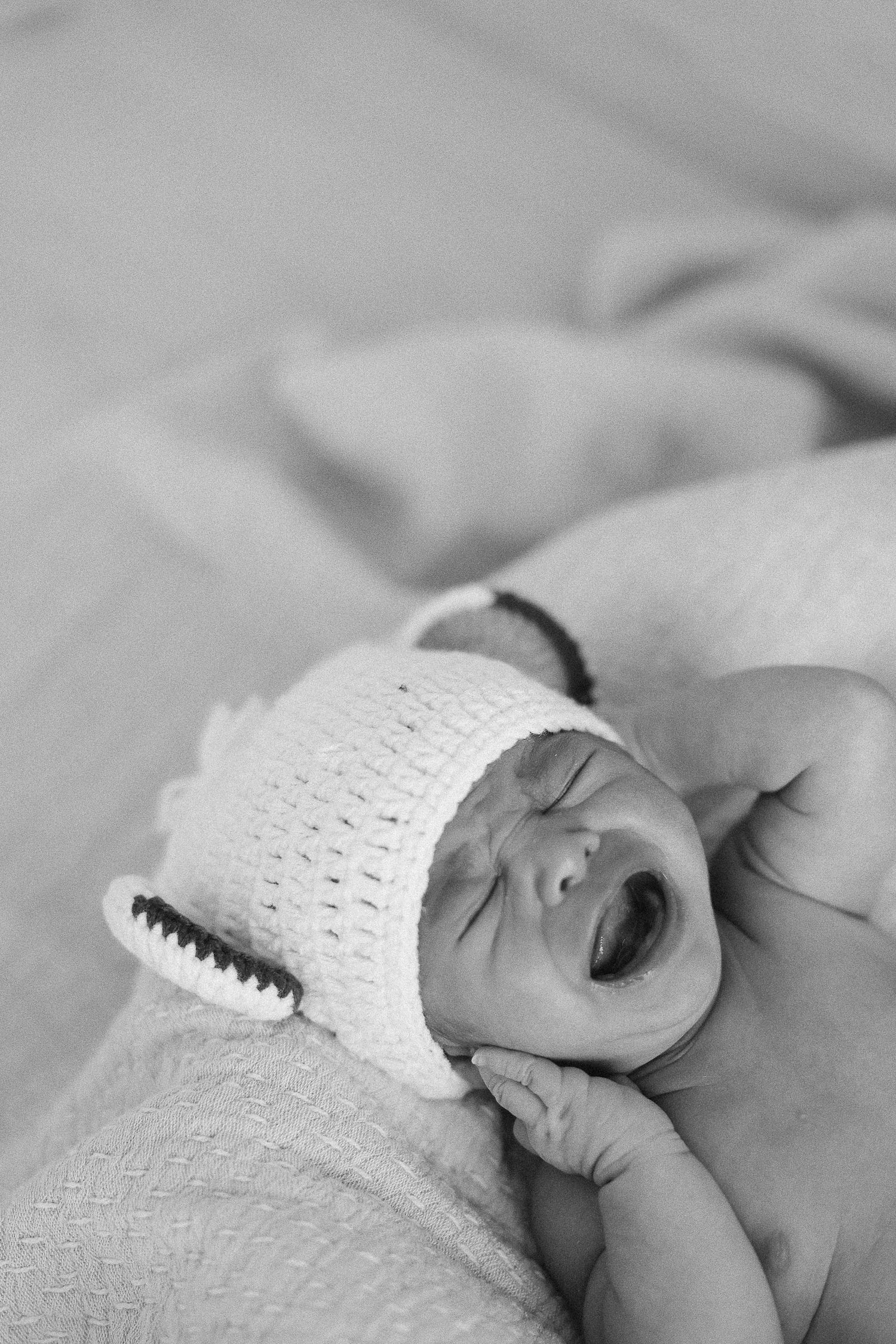 A sleeping newborn baby wearing a white knit hat is shown in a black and white photo series.