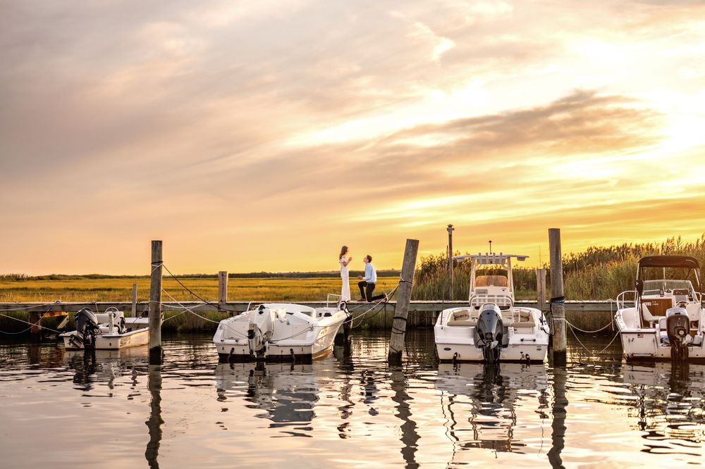 Fishing boats docked at marina during dramatic golden sunset with cloudy sky and calm water reflections.