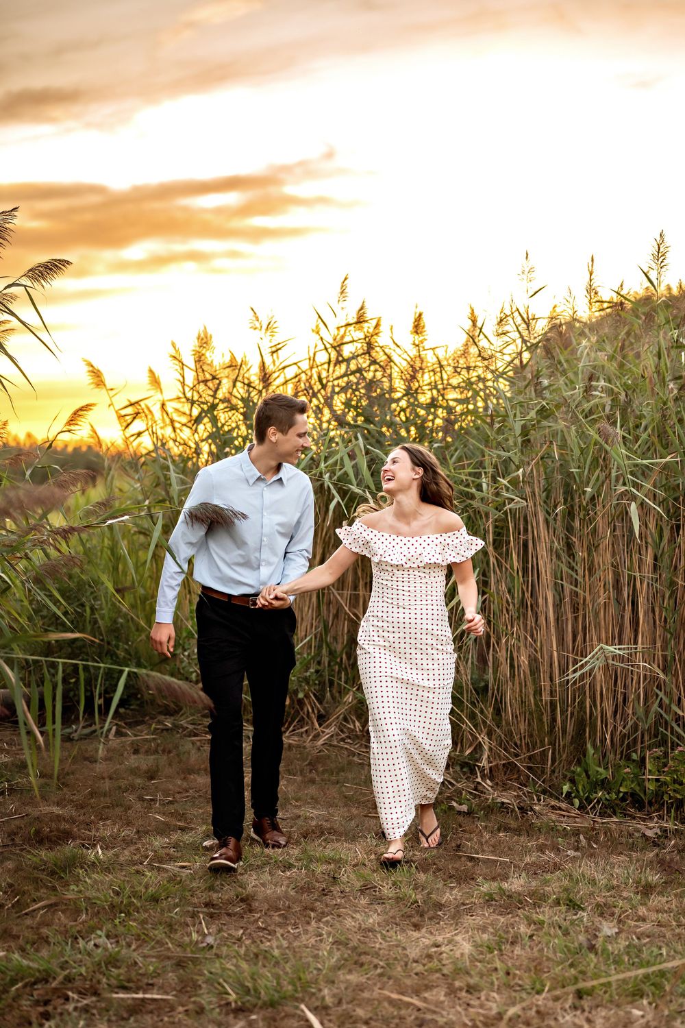 Couple running together through a field of tall grass during golden sunset.