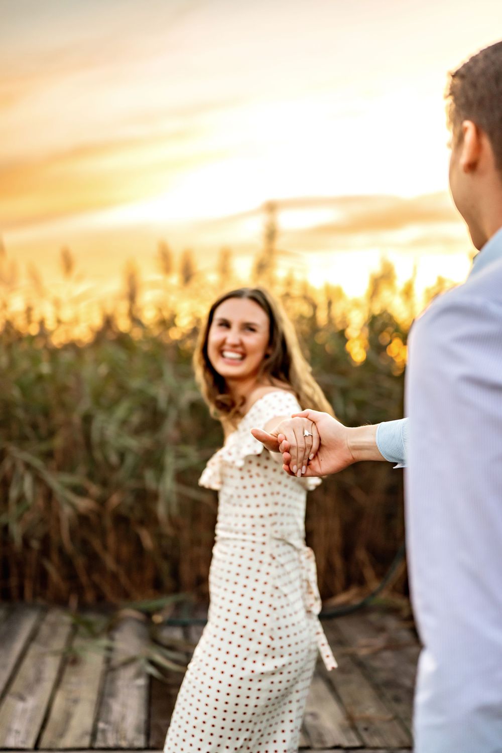 A couple shares a playful moment during sunset in a cornfield, creating a warm and romantic engagement photo.
