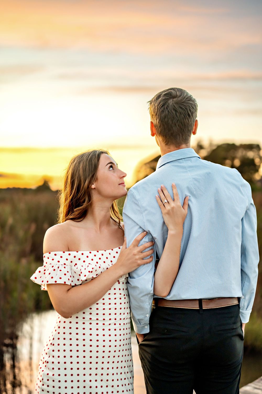 A couple dressed in white and blue stands together against a scenic sunset while showcasing a sequence of romantic poses.