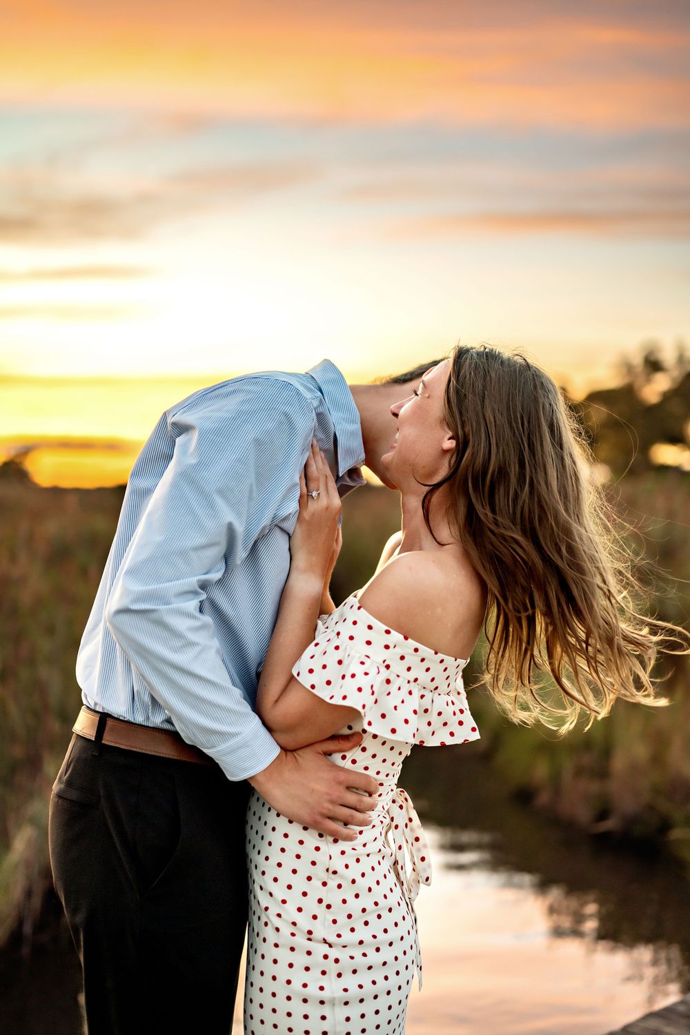 A romantic sunset silhouette shows a couple embracing tenderly by a tranquil pond.