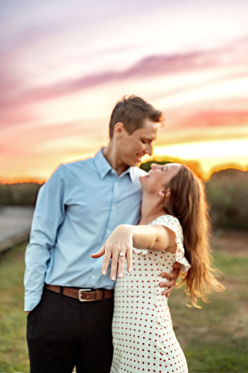 Romantic couple dances together at sunset in a field as her polka dot dress twirls through golden light.