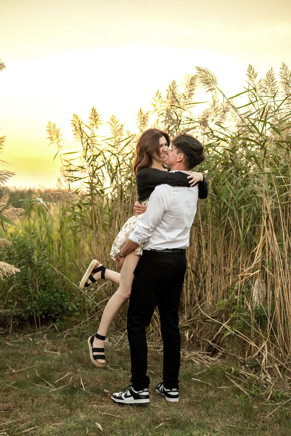A romantic couple embraces in a field of tall reeds during golden hour sunset.