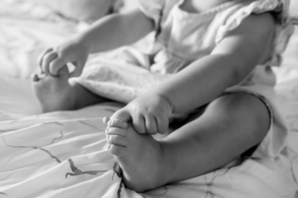 toddler holds her own feet while sitting on a bed in fort worth home photo session