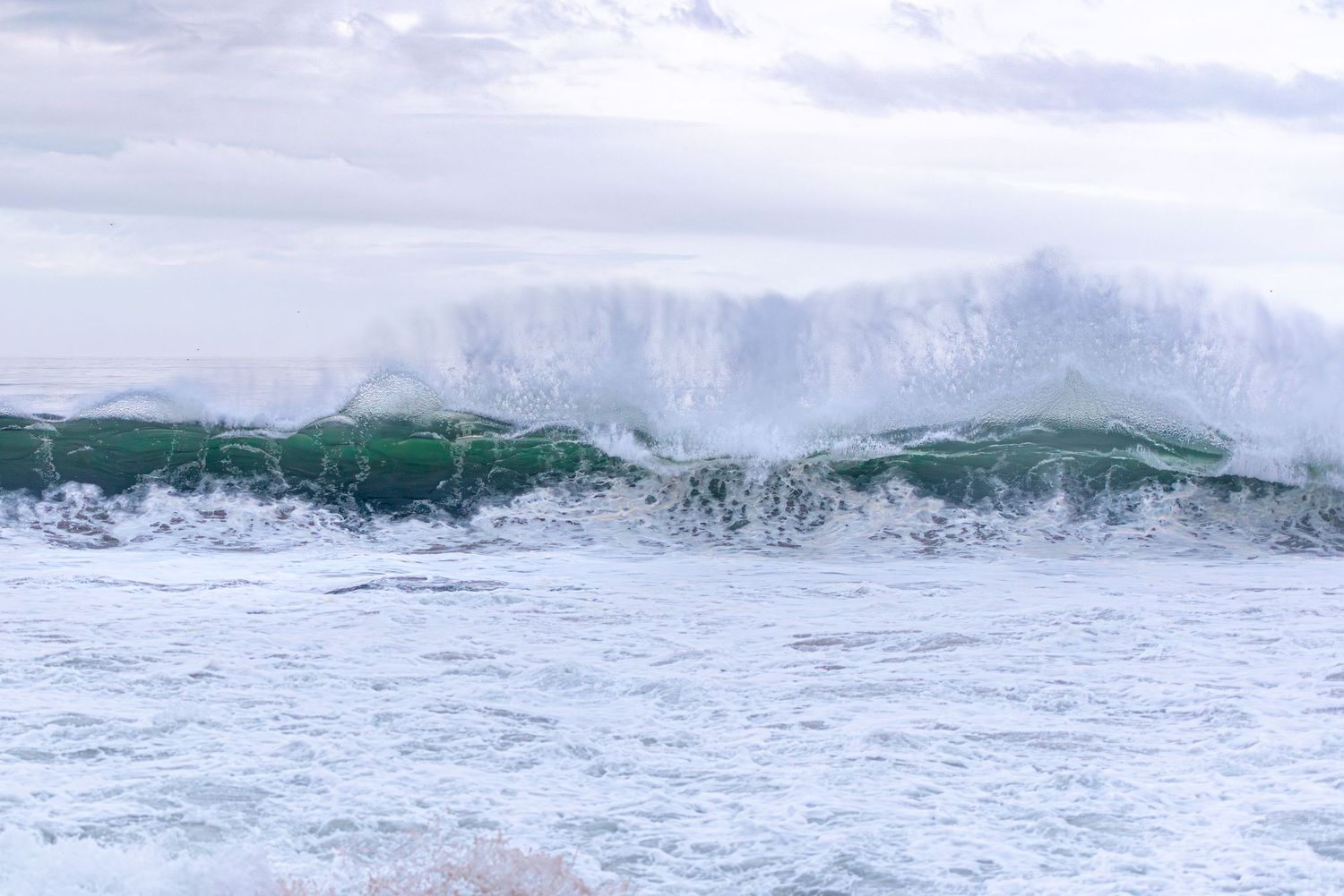 Ocean waves roll in during sunset creating a serene seascape with pink sky.
