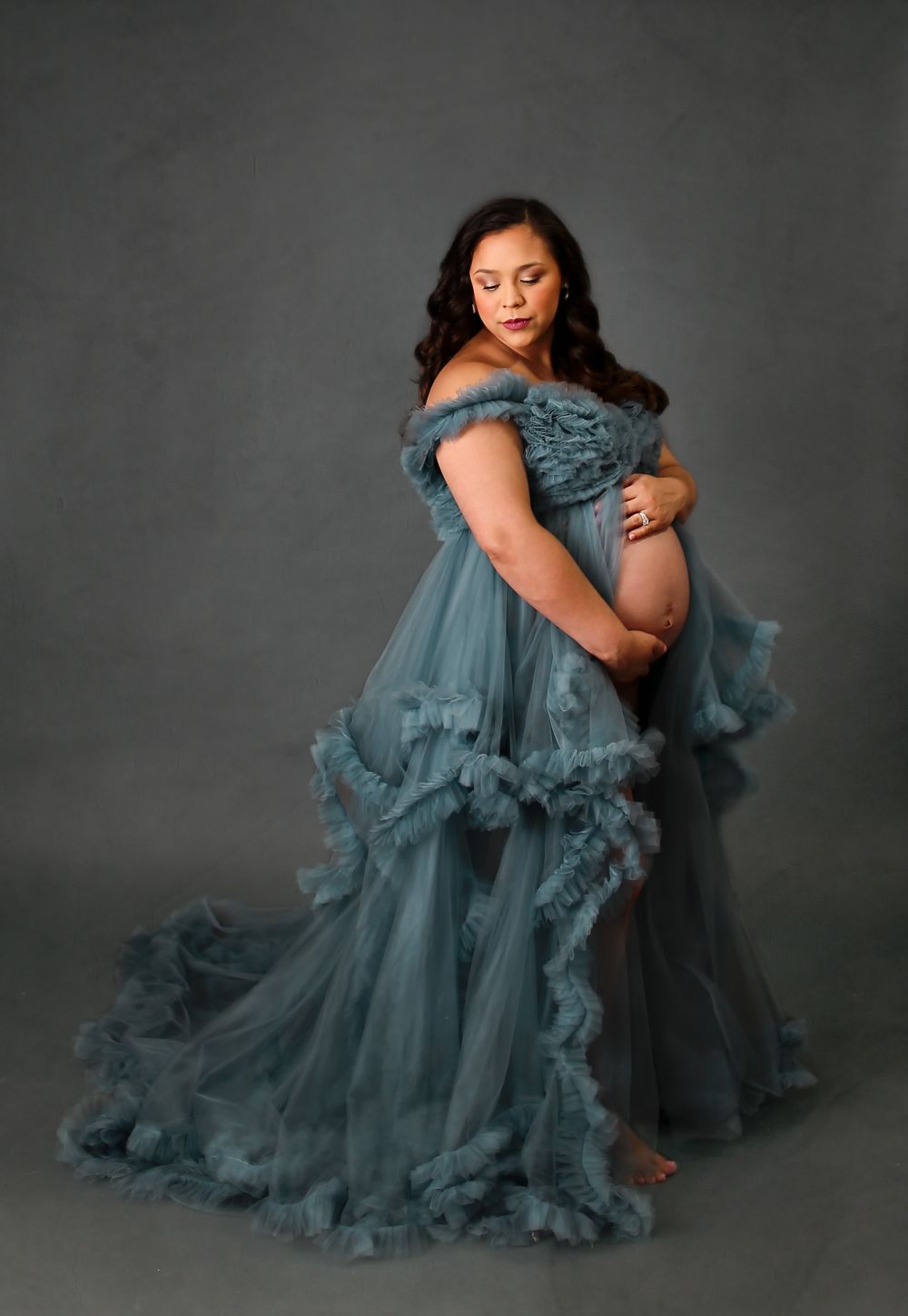 Pregnant mama in studio wearing a beautiful blue maternity dress posing for a maternity session while holding belly