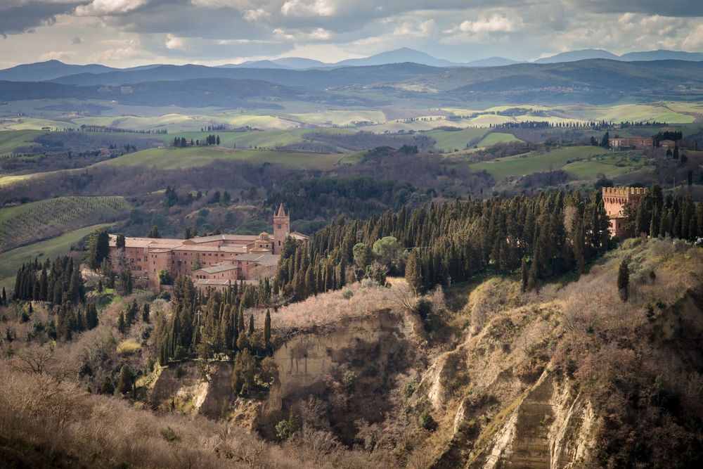 Rolling Tuscan hills dotted with cypress trees and medieval villages stretch across a scenic countryside landscape.