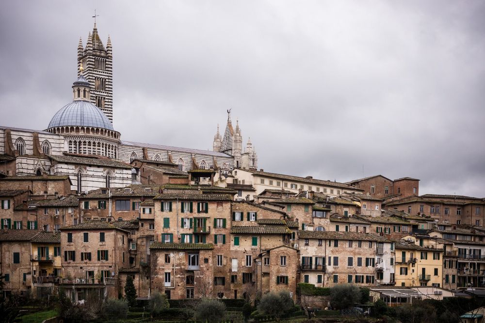 Panoramic view of Siena, Italy showing historic medieval buildings and the famous Duomo cathedral under cloudy skies.