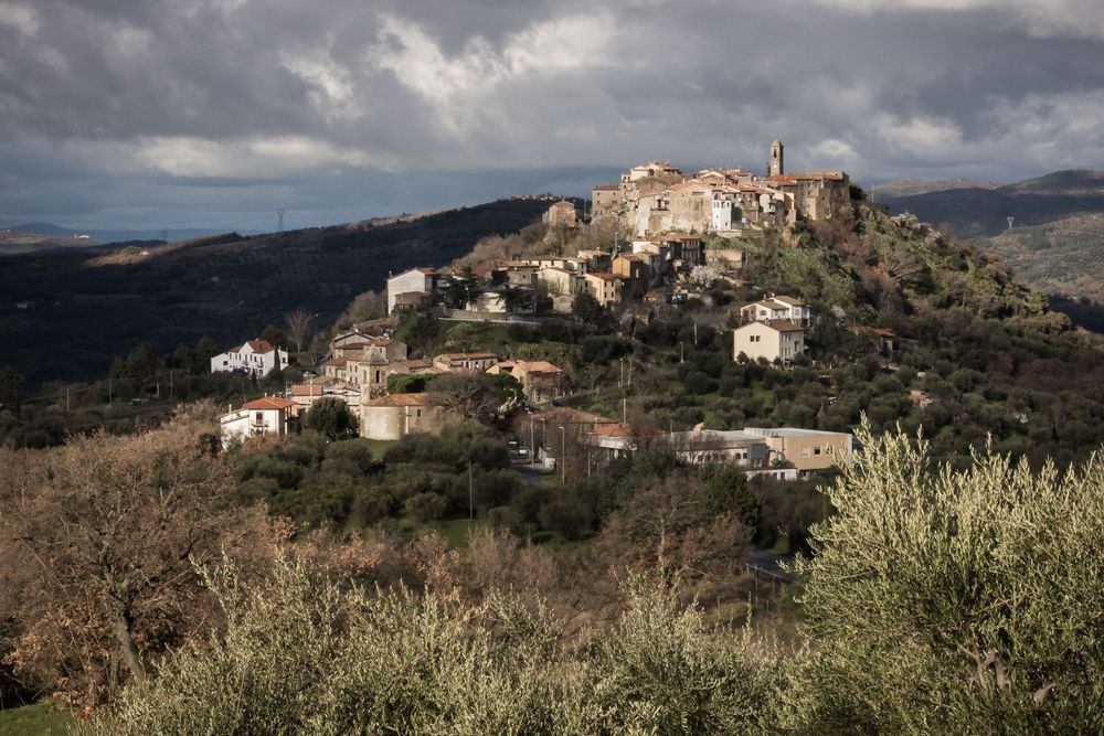 A panoramic view of traditional hilltop villages in Corsica with dramatic mountainous landscape and cloudy skies.