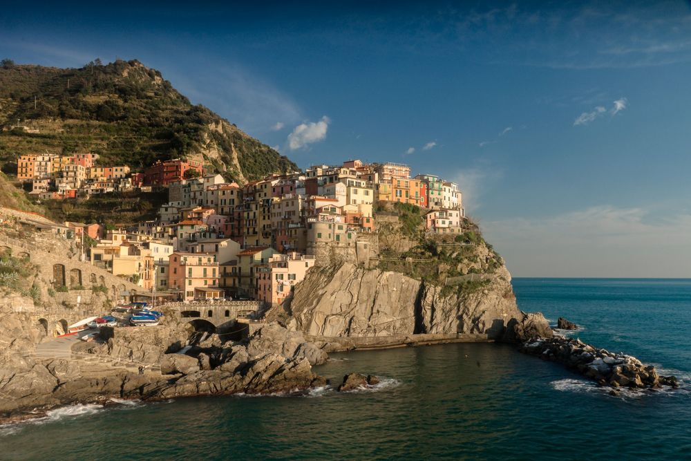 Panoramic view of colorful coastal buildings in Cinque Terre perched along the rugged Italian Riviera cliffside at sunset.