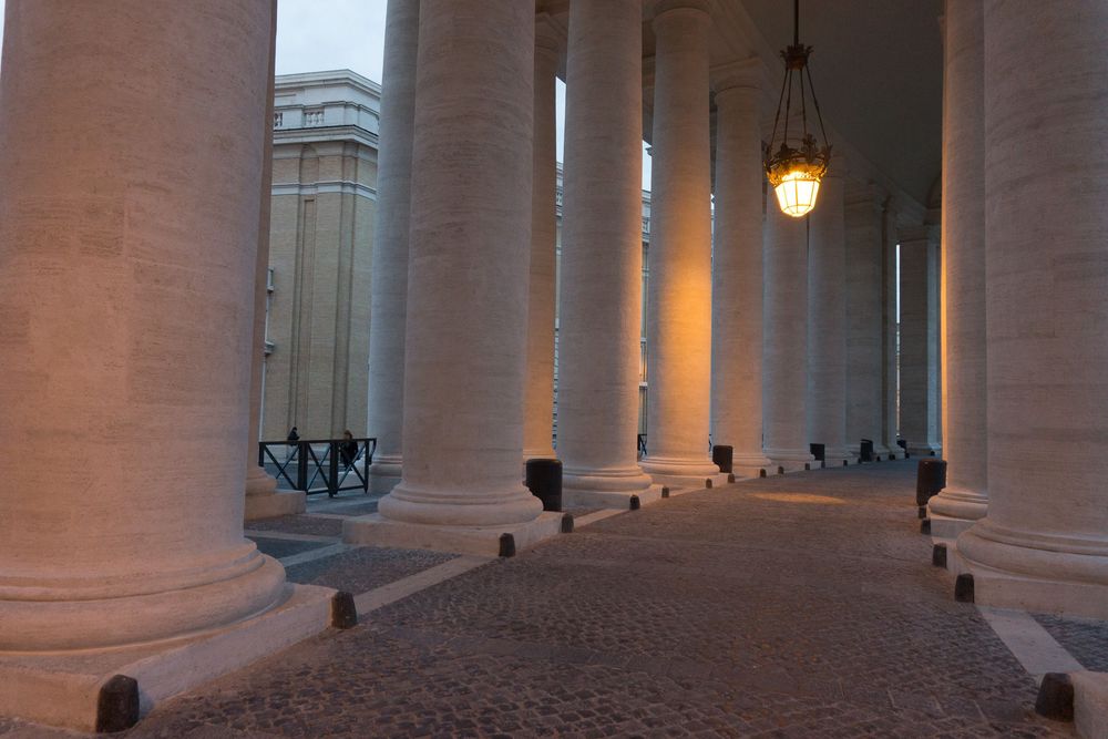 Long colonnade walkway with stone columns and ornate ceiling at St. Peter's Basilica in Vatican City.