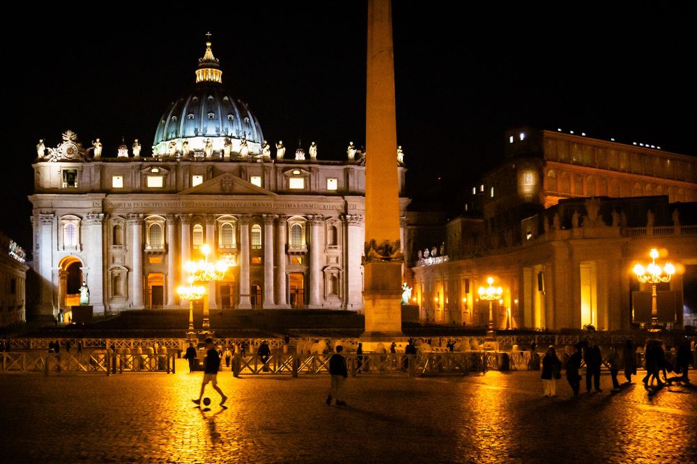 Night view of St. Peter's Basilica and Square in Vatican City illuminated by golden lights.