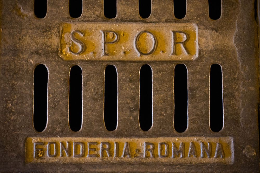 Ancient Roman copper sign with the letters SPOR and patina texture visible against a rustic wall.