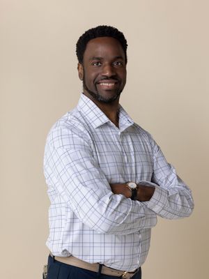 Professional studio portrait showing man in white checkered button-down shirt with crossed arms against neutral backdrop.