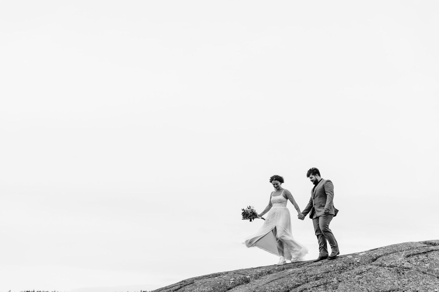 A wedding couple climbs a hill in silhouette during a scenic black and white outdoor photo session.