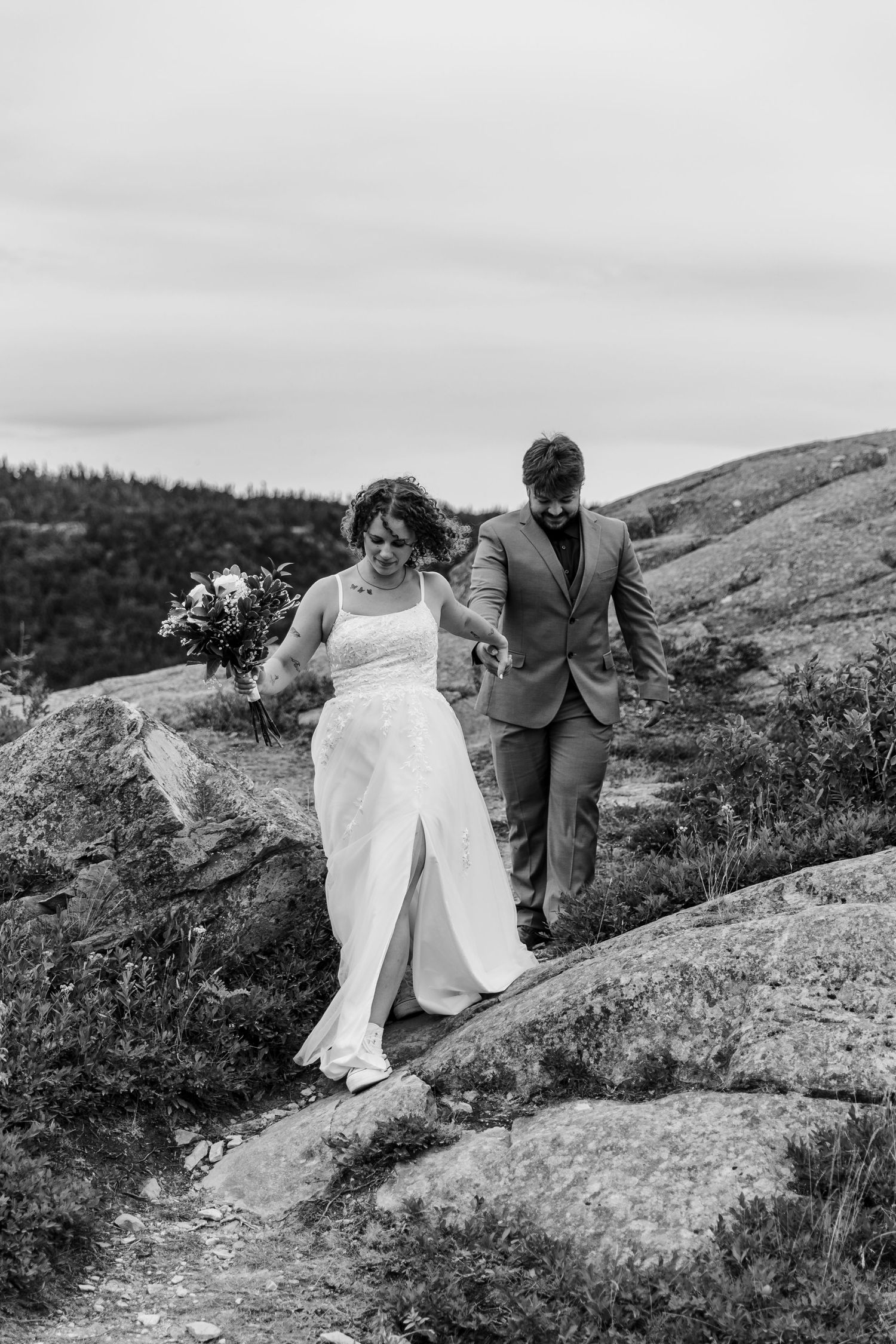 Newlywed couple climbing up rocky terrain in black and white at their mountain wedding photoshoot.