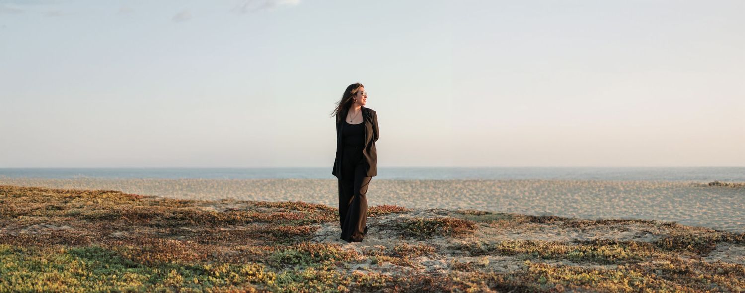 Silhouette of person standing on rugged coastline at sunset with dramatic sky and ocean view in background.