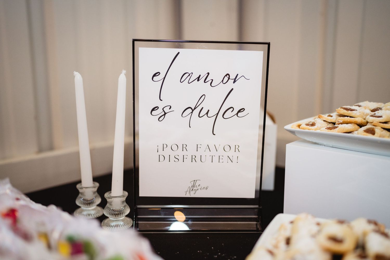 Wedding reception decor with table settings, framed signs, and white candles in an elegant indoor venue.
