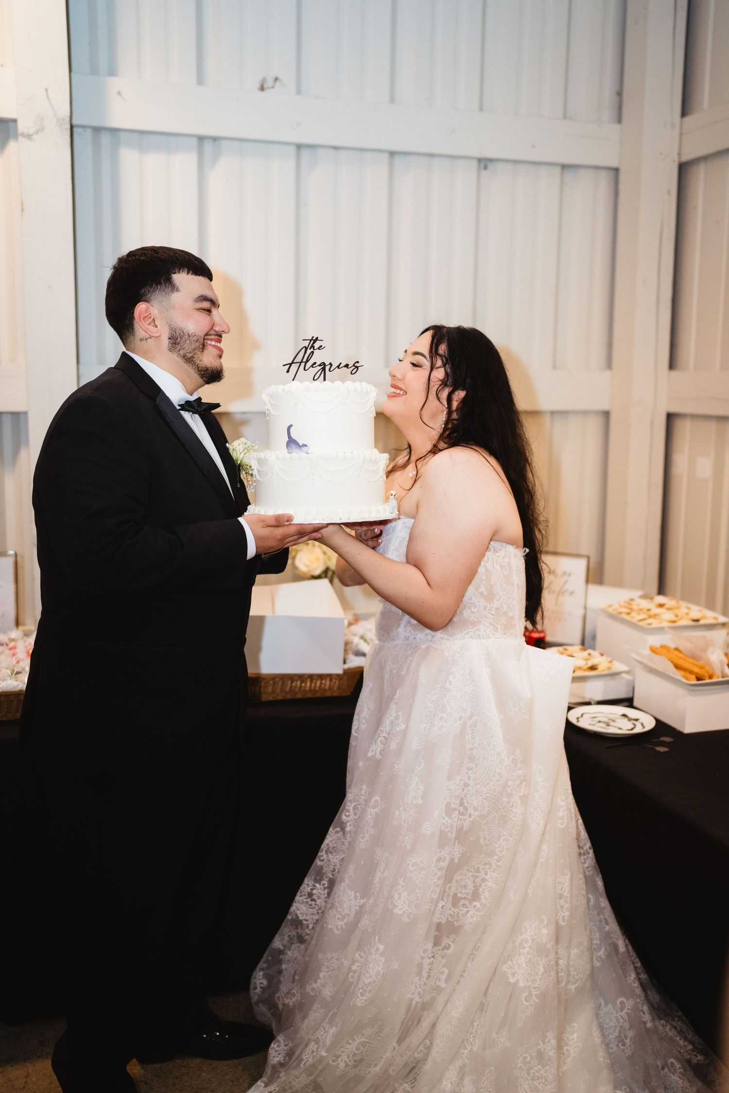 Newlywed couple laughing while feeding each other wedding cake at their reception celebration.