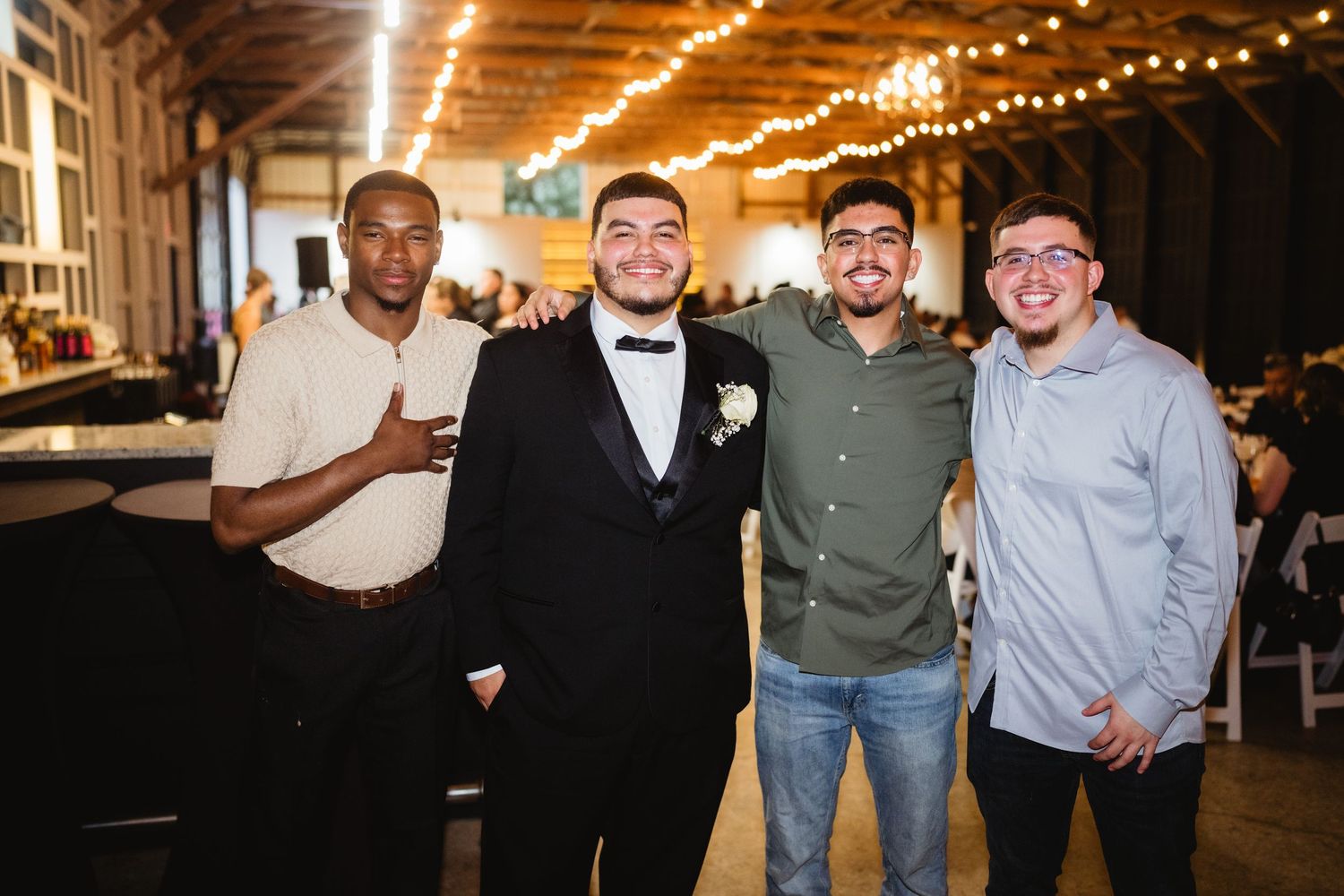 People smiling and posing together at what appears to be a social event with string lights in the background.