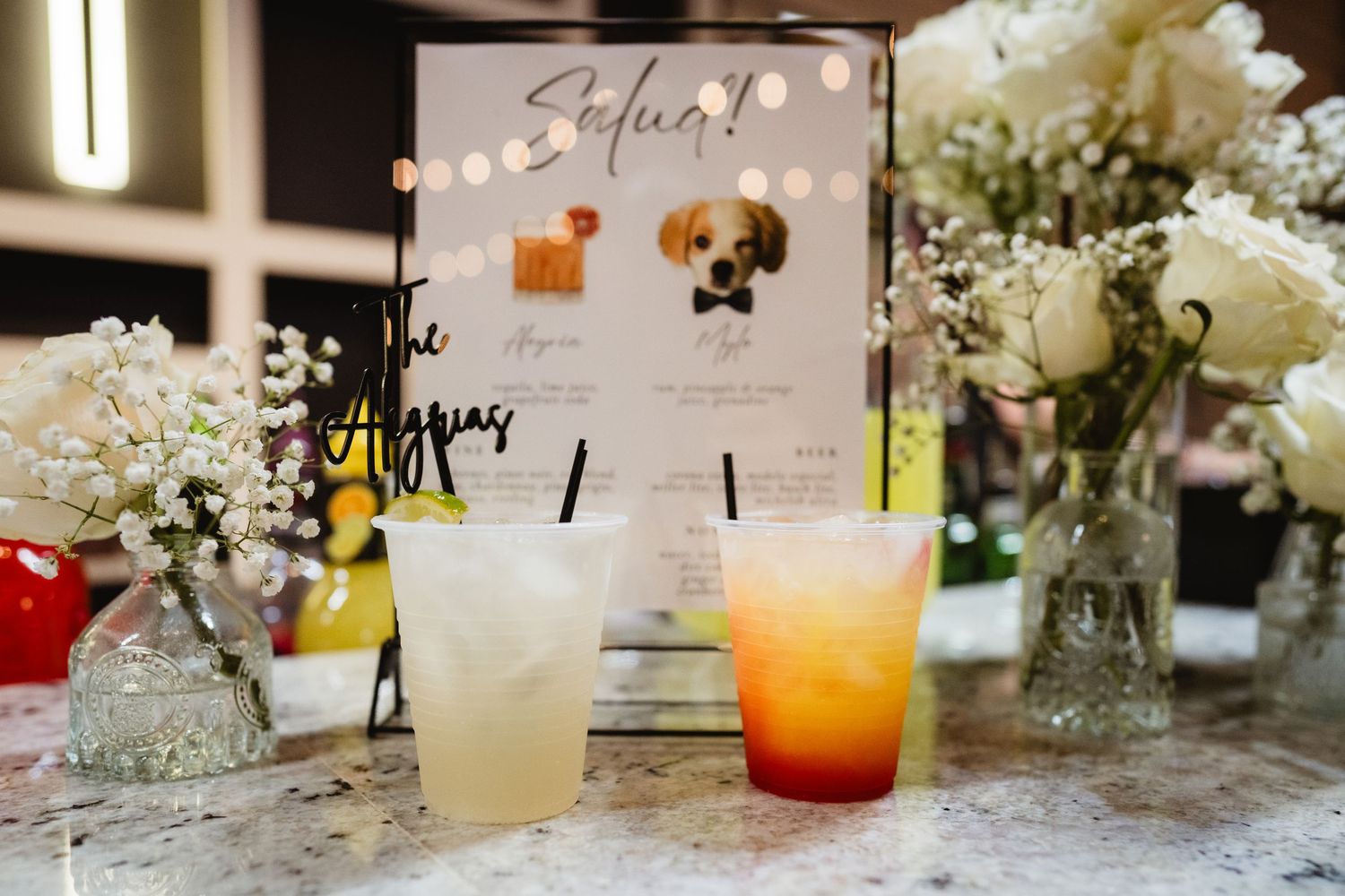 Colorful cocktails and delicate white flowers adorn a table setting with a cocktail menu display.