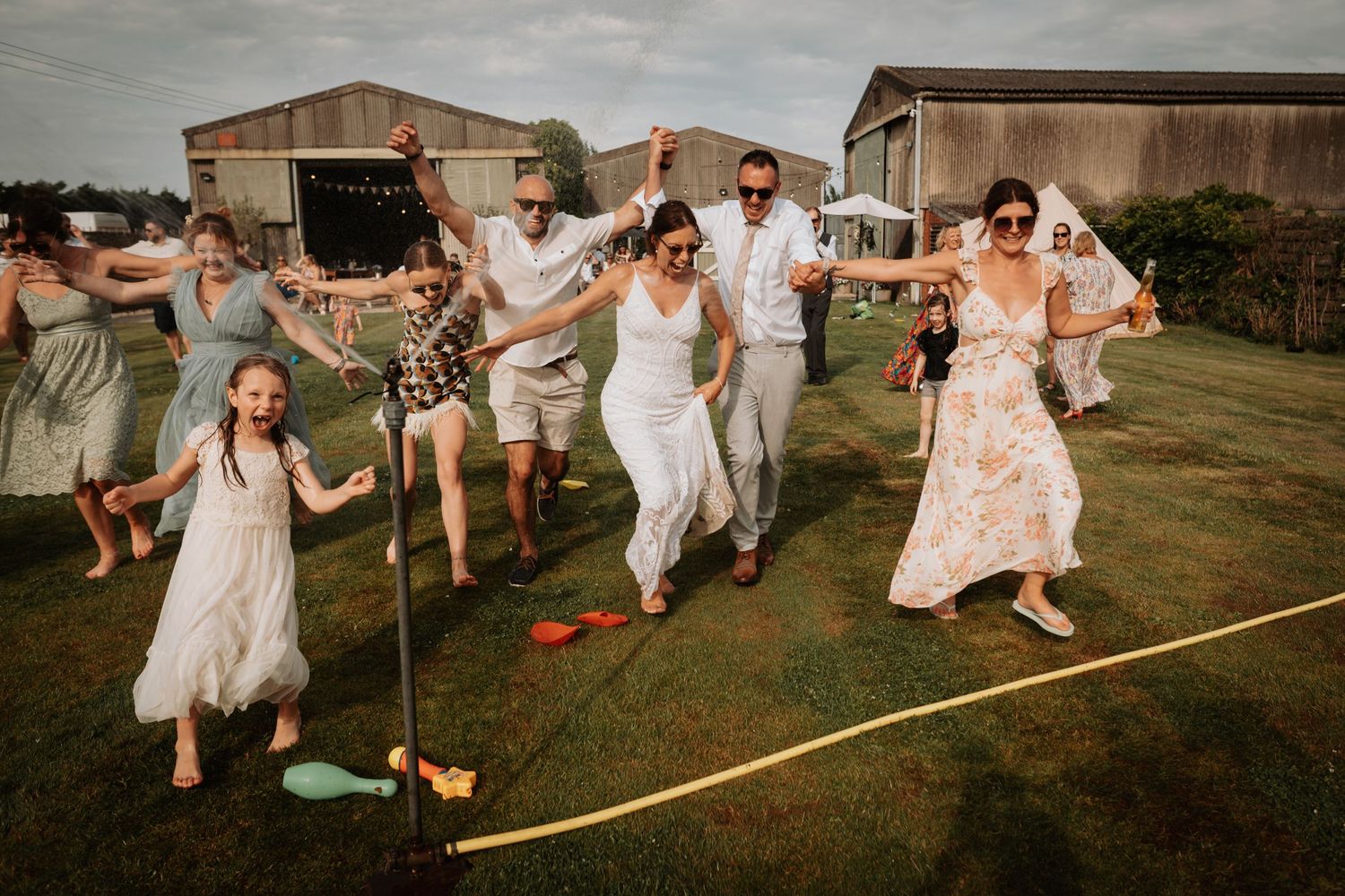 Wedding party jumps and dances joyfully on putting green during outdoor rustic farm celebration.