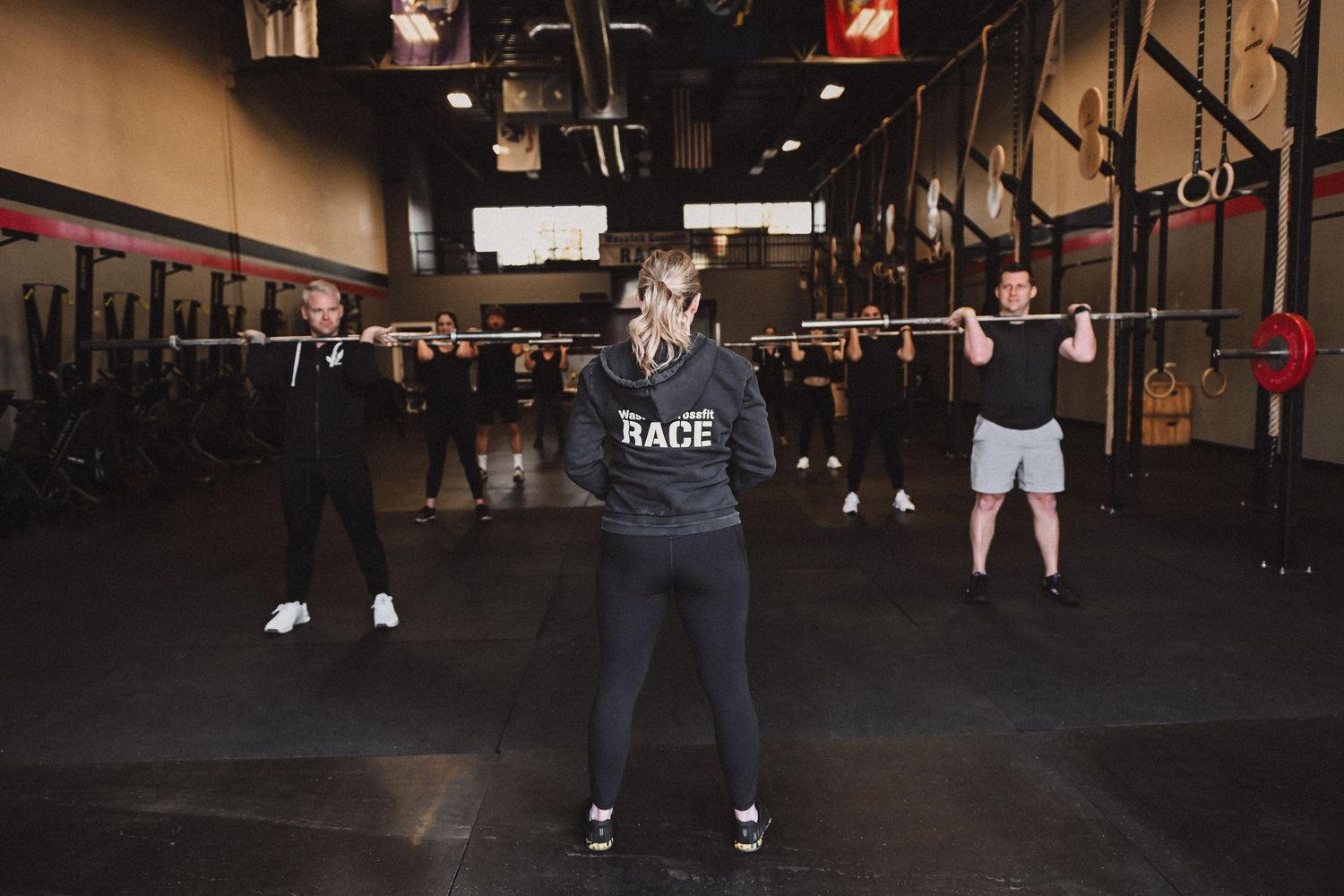 Gym members stretching and exercising together during a CrossFit class in a dark warehouse-style gym setting.