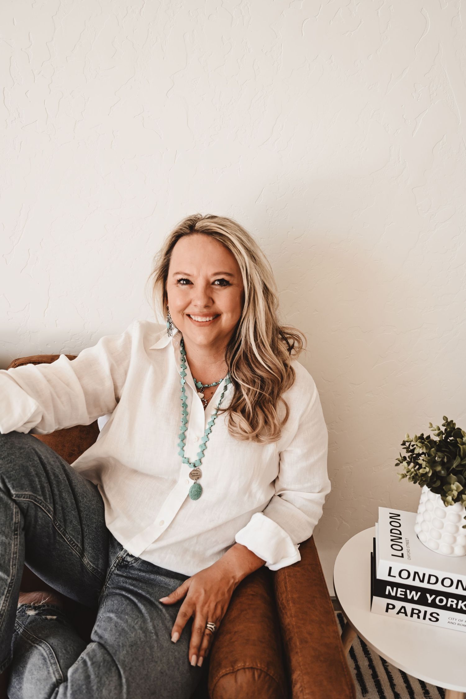 Lifestyle photo shoot with white sweater and turquoise necklace on brown leather couch.