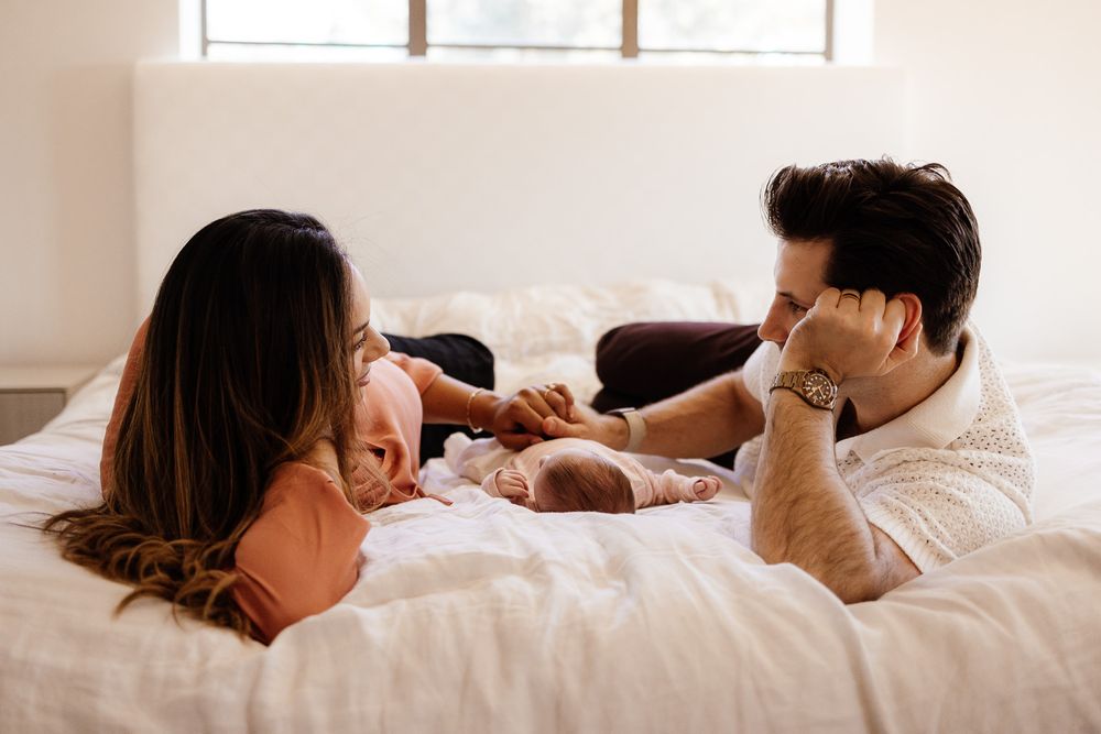 Parents lie on their bed with their newborn baby in between them in Los Gatos in-home lifestyle photography session