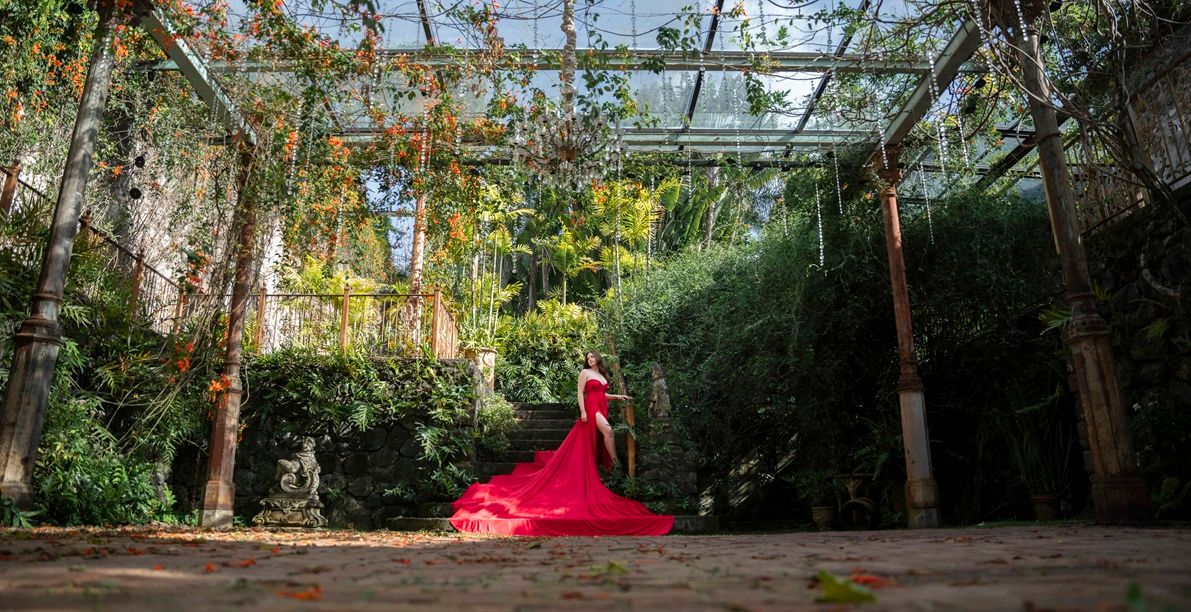 A red flying dress flows through an archway in a lush garden setting Maui, Hawaii