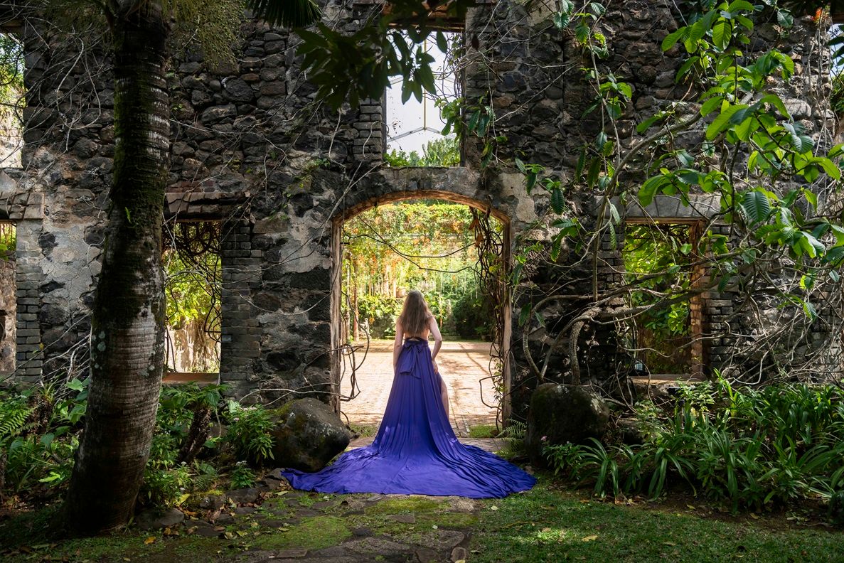 A purple flying dress flows dramatically through stone ruins surrounded by greenery Maui, Hawaii