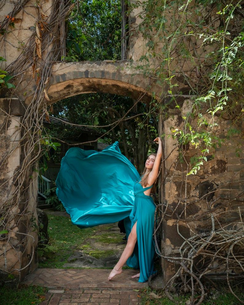 A turquoise Flying dress flowing fabric creates movement against historic stone architecture Maui, Hawaii