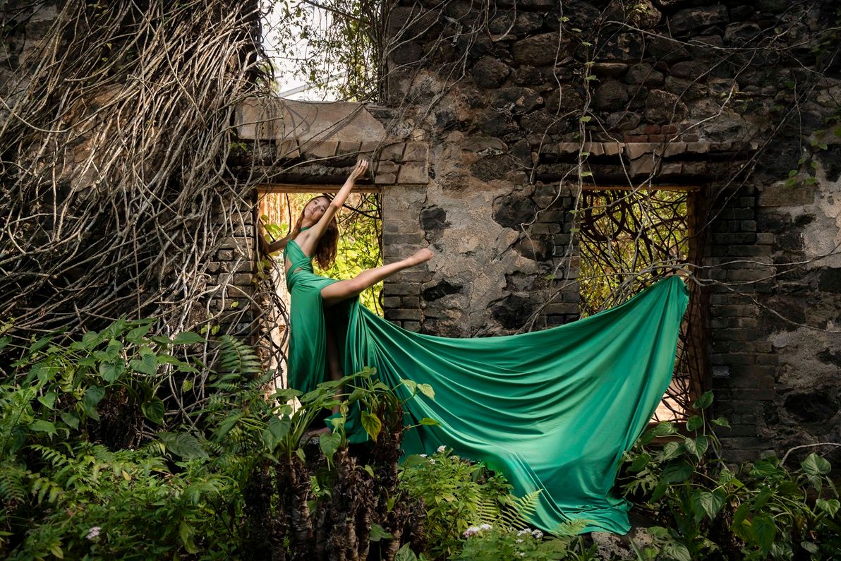 Flying dress emerald green fabric creates dynamic shapes against stone walls and vegetation, Maui, Hawaii