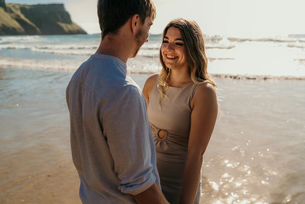 Two people enjoying a romantic moment together on a sunny beach with waves and cliffs in view.