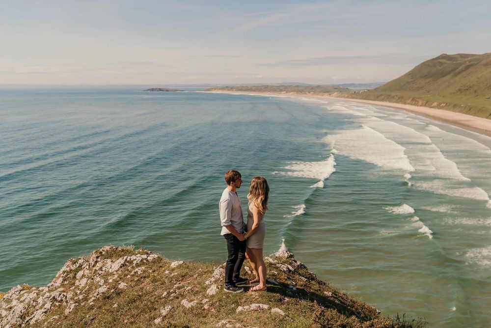 Coastal wedding photography scene overlooking dramatic ocean waves and cliffs at sunset along a scenic beach.