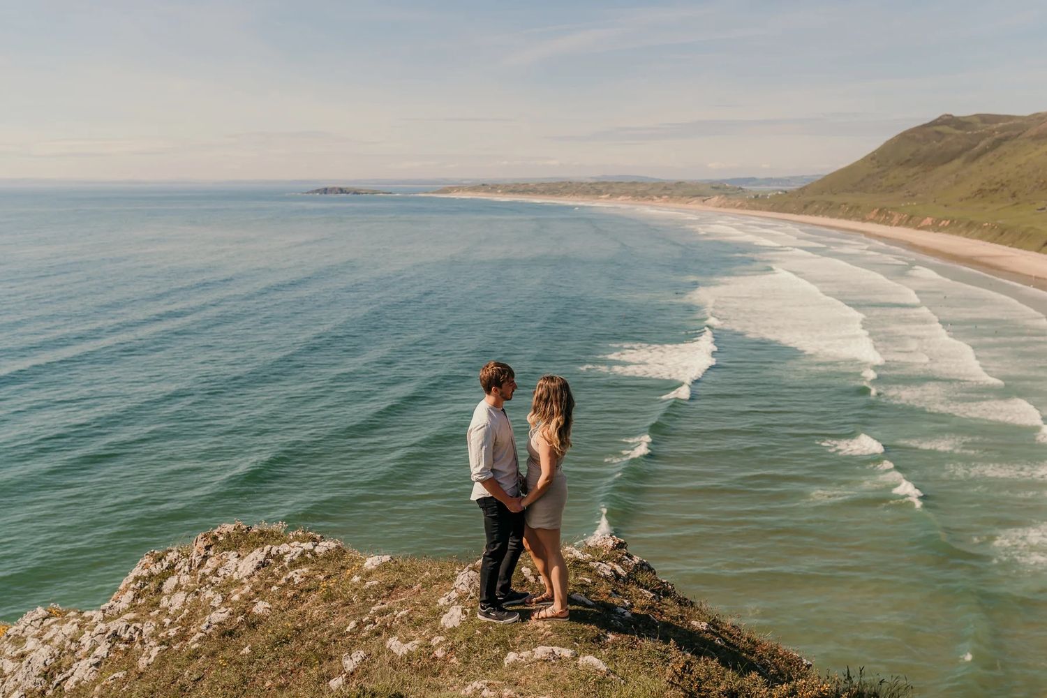 Coastal wedding photography scene overlooking dramatic ocean waves and cliffs at sunset along a scenic beach.