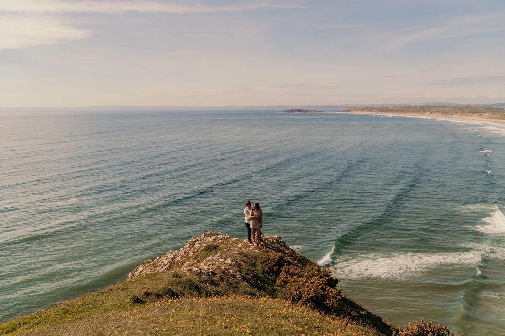 Scenic aerial view of Portugal's rugged coastline with waves crashing against cliffs and a distant beach stretching into horizon.