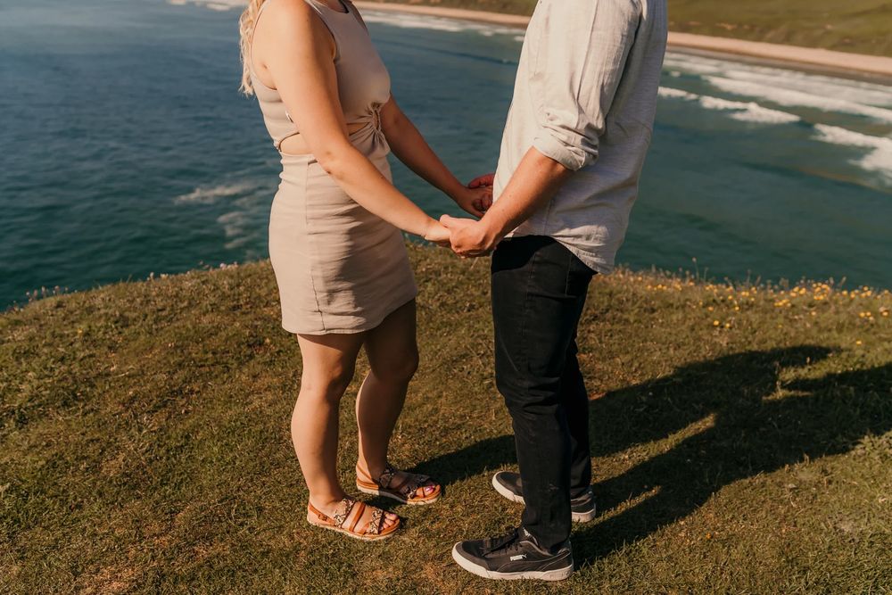Romantic couple embraces on a scenic coastal cliff overlooking the blue ocean on a sunny day.