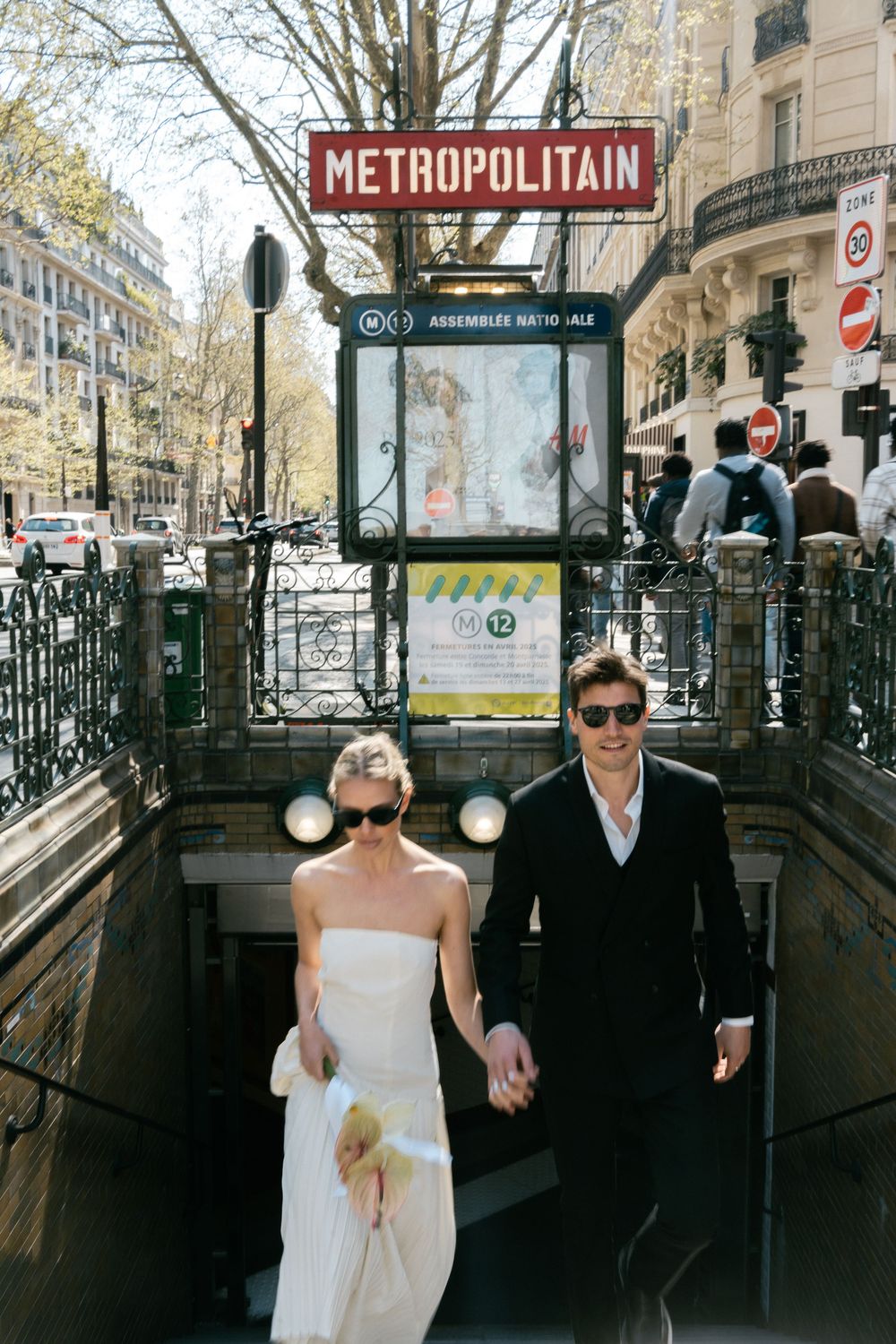 A couple in formal attire walking up steps from a Paris Metro station marked by the iconic Metropolitain sign.