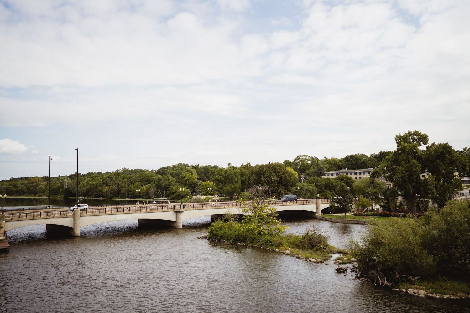 A panoramic view of a river dam with green trees along the shoreline and boats docked in the calm waters.