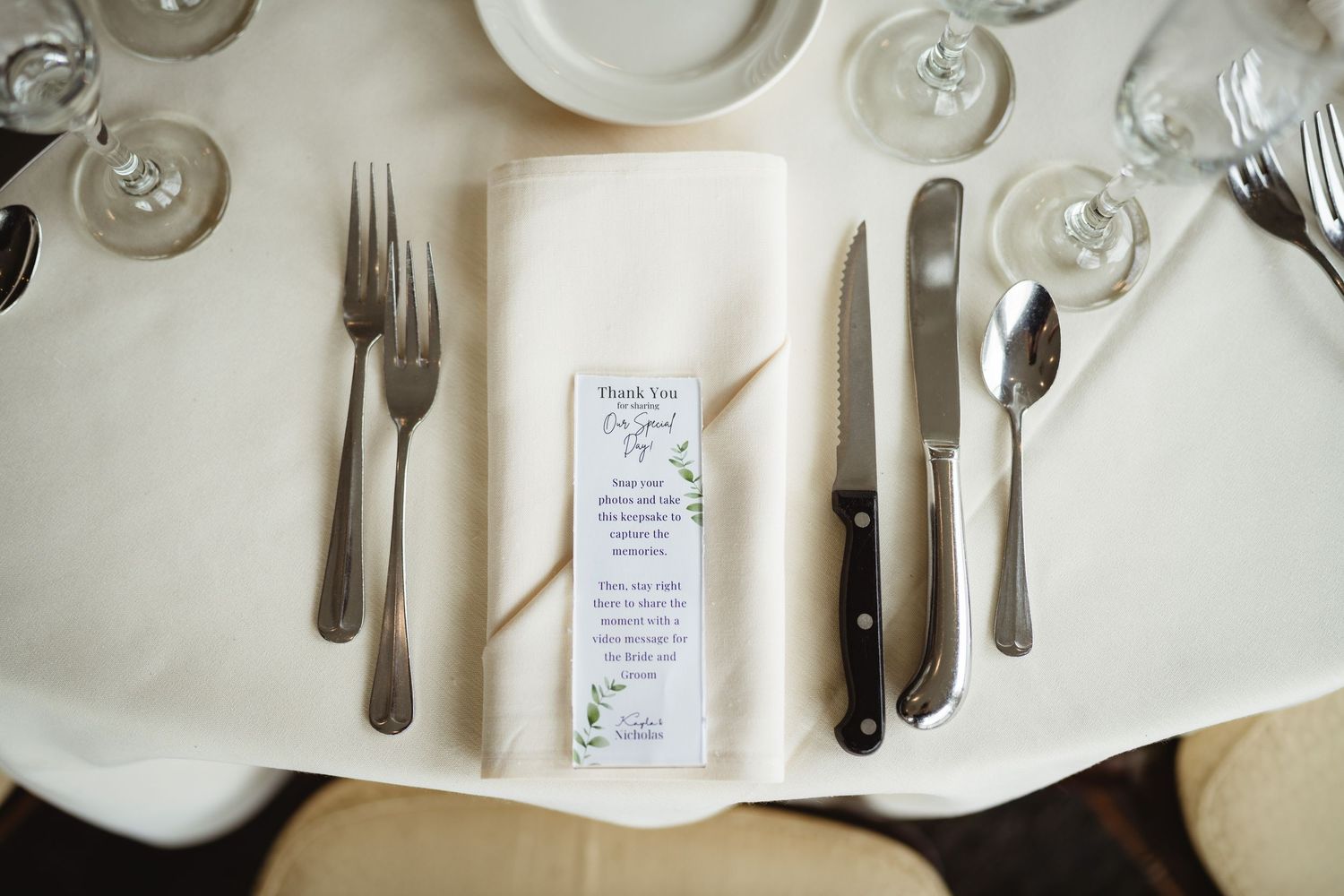 An elegant table setting features crisp white plates, polished silverware, and menu cards arranged on a light beige surface.