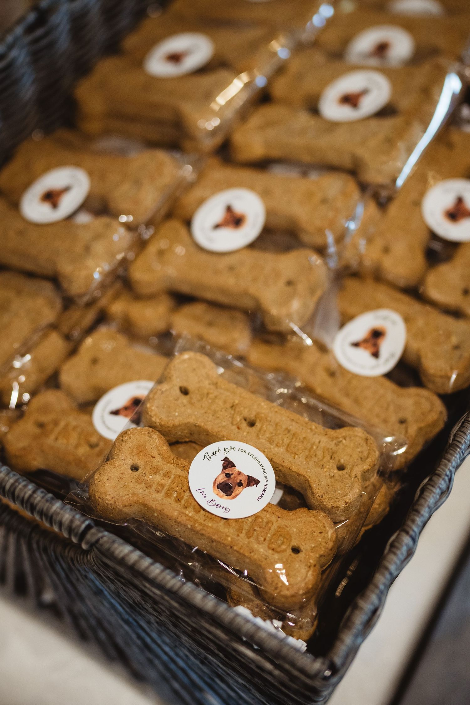Bone-shaped dog treats with white frosting arranged in rows on a dark woven tray reveal their artisanal bakery presentation.