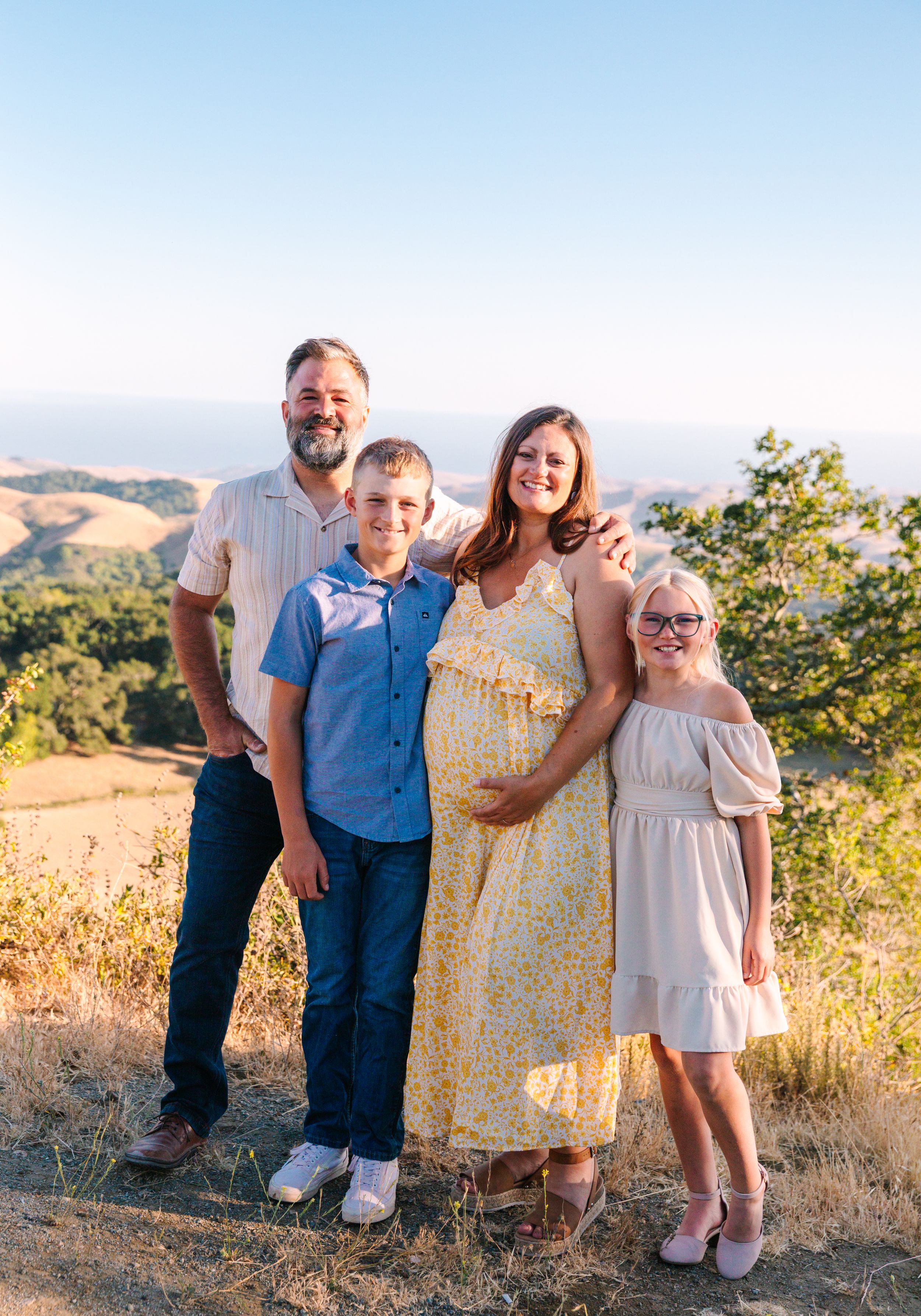 Family portrait taken on a hilltop during golden hour with mountains in the background.