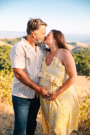 A couple shares an intimate moment while standing on a hilltop overlooking a scenic valley during golden hour.
